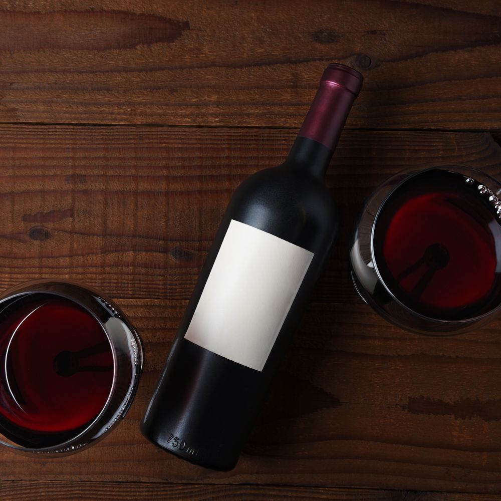 Study: a red wine bottle with a blank label, laid on dark wood between two glasses